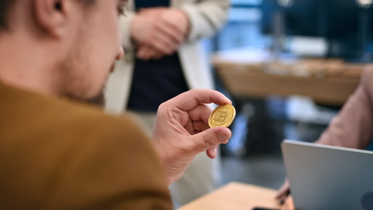 Worker holding a physical coin in an office. Gadgets and papers on the table. Slow motion