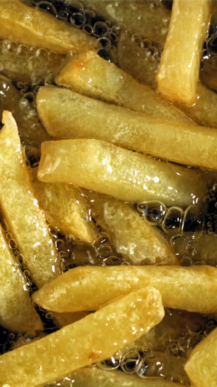 Patatas fritas doradas cocinándose en aceite hirviendo burbujeante
