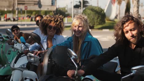 trendy young friends on scooters waving at camera