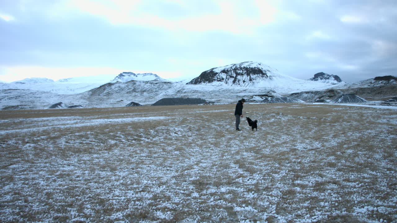 Stable shot shows a young man and his energetic dog playing on a snow covered field
