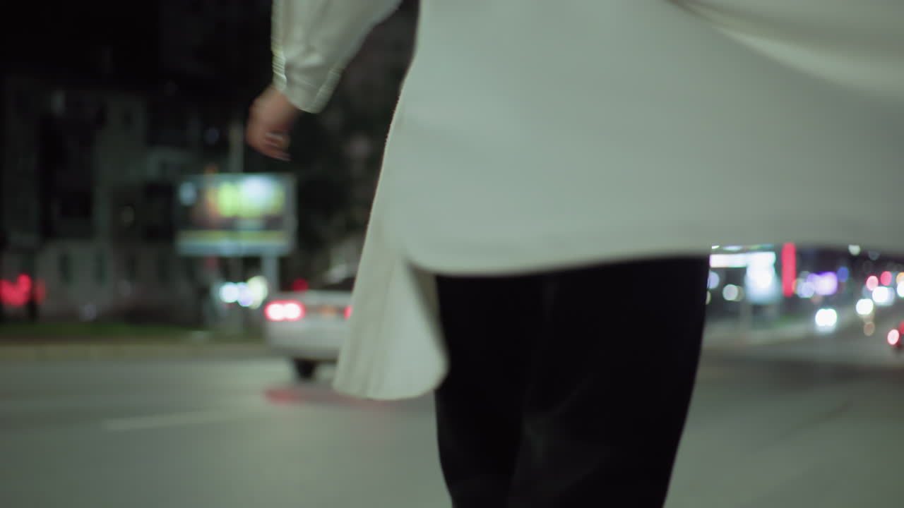 Girl full of joy turns around near pole on illuminated night street while car drives by in background, surrounded by urban lights and soft glow from buildings