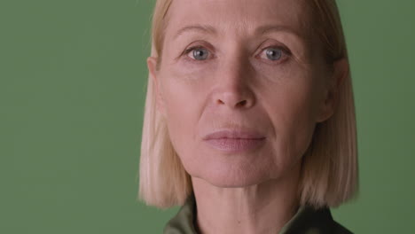 Close-Up-View-Of-Blonde-Mature-Woman-With-Blue-Eyes-Looking-At-Camera-On-Green-Background