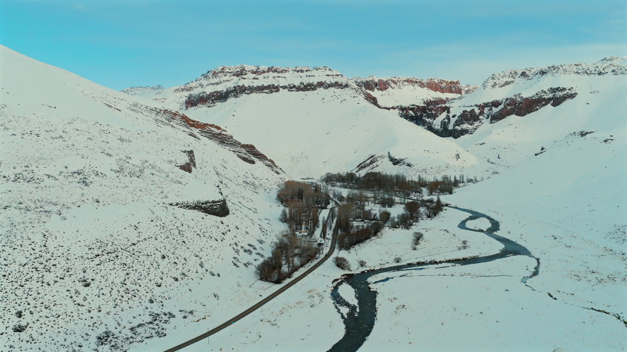 Aerial view of snowy mountains and winding river at Paso Pehuenche, Mendoza, Argentina.