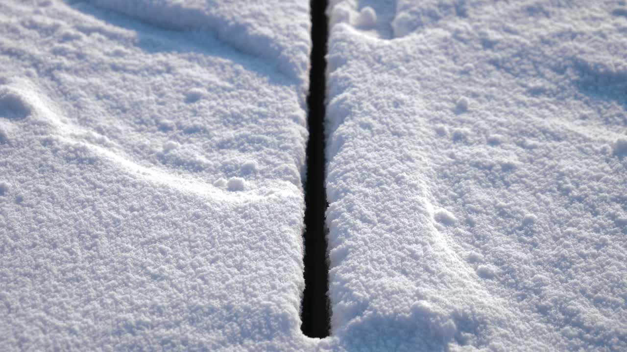 A precise cut line in thick ice was created by an industrial cutting machine on the frozen Songhua River in Harbin. The snow-covered surface contrasts with the deep, dark separation.