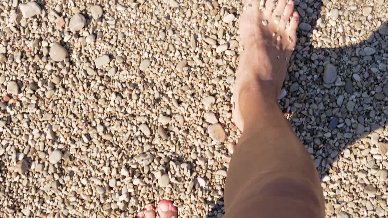Persona che cammina a piedi nudi su una spiaggia di ciottoli ed entra in acqua di mare cristallina