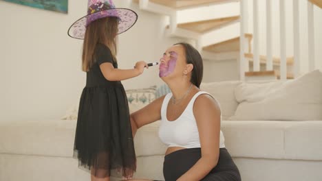 little girl in witch hat applying makeup on pregnant mother for halloween