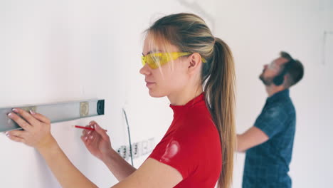 girl in goggles checks wall level and man listening to music