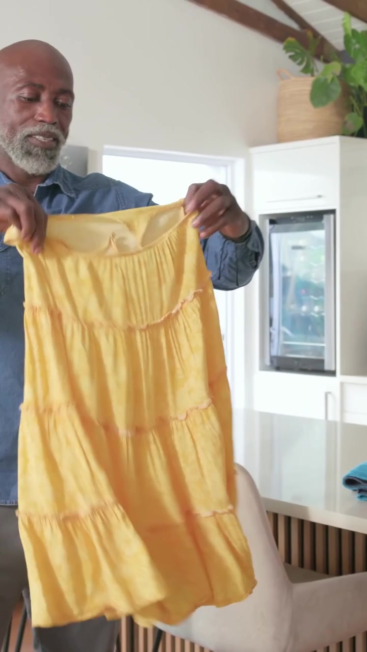 Vídeo vertical: Levantando vestido amarelo da cesta, homem dobrando, empilhando toalha listrada para arrumar a casa