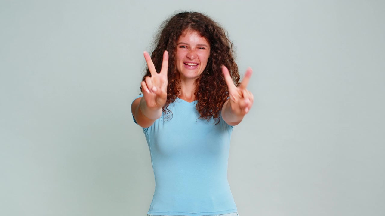 Giovane donna felice che mostra il segno della vittoria e della pace con la mano, con espressione allegra, positiva, gioiosa e ottimista
