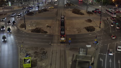 Forwards-tracking-of-tram-driving-across-large-roundabout.-Tilt-up-reveal-of-evening-traffic-on-multilane-road-in-city.-Warsaw,-Poland