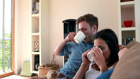 una pareja joven y linda relajándose en el sofá con café.