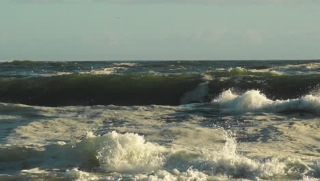 las olas violentas del mar que crean salpicaduras y espuma durante la tarde dorada - pan shot