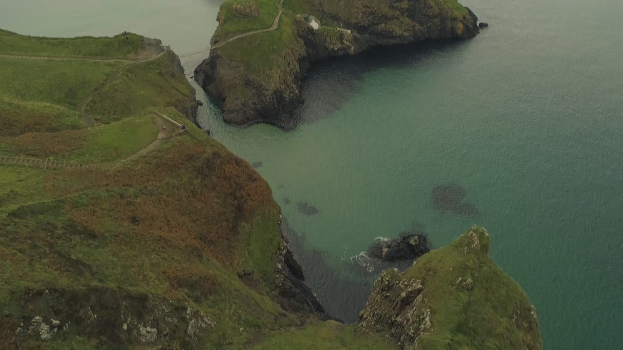 aerial de un hombre de pie en el borde de un acantilado de montaña en la costa del océano atlántico carrick una rede irland inclinándose hacia abajo en las profundidades