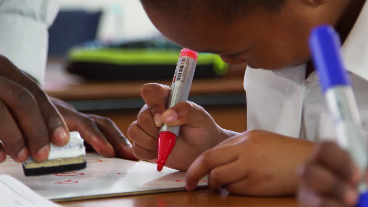 Teacher cleaning elementary schoolgirl's whiteboard