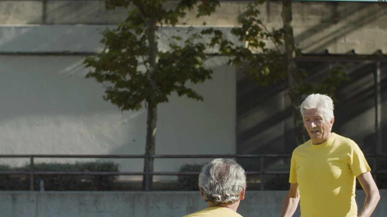 felices deportistas mayores de pelo gris entrenando juntos y golpeando la pelota con la cabeza en el estadio