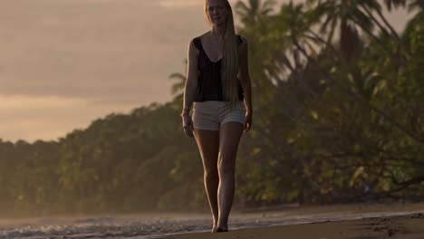 a serene moment as a woman walks barefoot along the golden shores of uvita beach during sunset, with the warm light casting long reflections on the wet sand and the jungle in the background