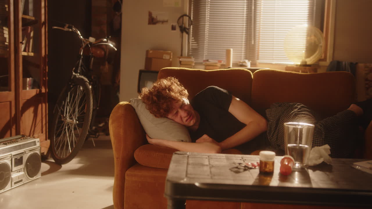 우울 한 남자 가 소파 에 누워서 따뜻 한 조명 을 받은 방 에서 감정적 으로 울고 있다