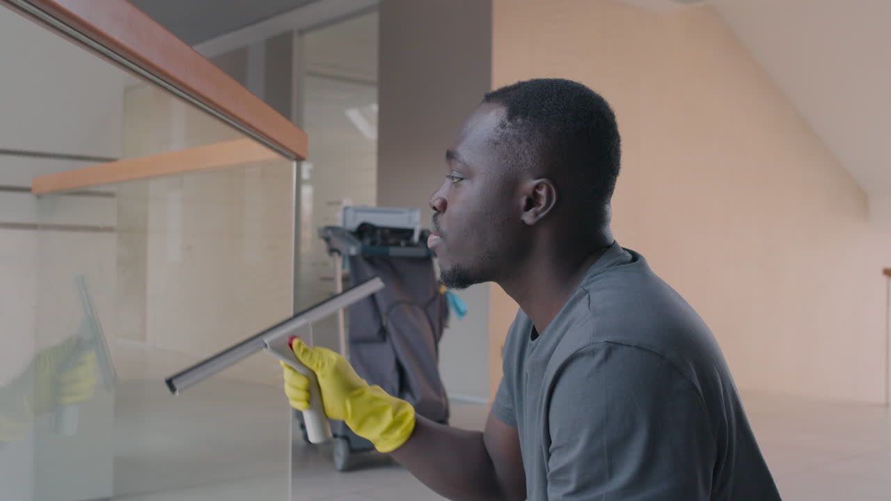 vista lateral del hombre de la limpieza con guantes limpiando la barandilla de la escalera y los cristales dentro de un edificio de oficinas
