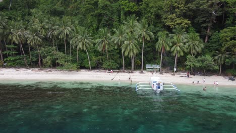 one filipino tour boat and people on tropical palm beach of pasandigan cove on cadlao lagoon, el nido