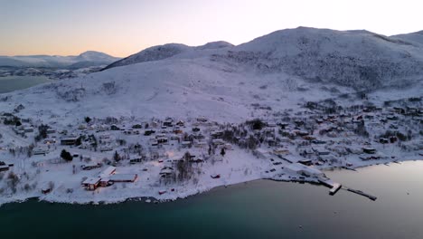 Flying-over-Norwegian-fjords-and-Ersfjordvegen-village-with-snowy-mountains-and-blue-sea