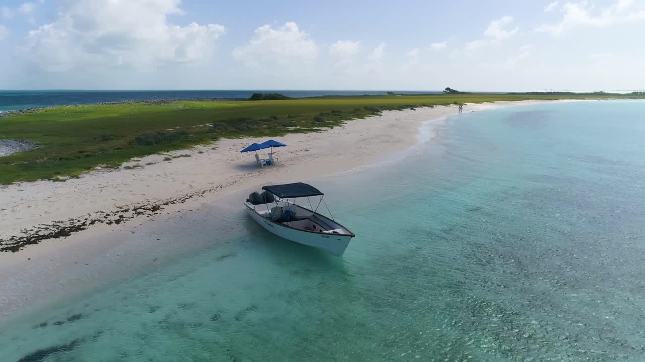 Romantic Sunset tropical beach with Boat and Two Beach Chairs. Drone shot turn around island.