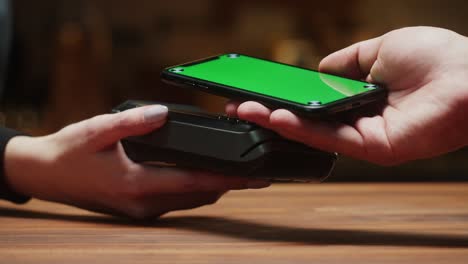 pagar por teléfono inteligente con pantalla verde cromada de primer plano. compras sin efectivo en un restaurante o café. concepto de pago sin contacto y sin contacto. tecnología nfc y terminal bancario.