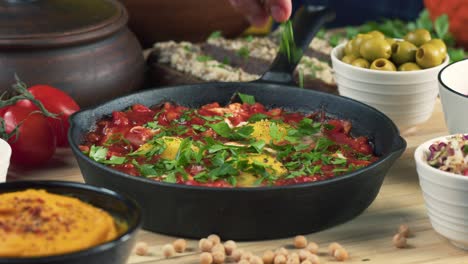 israeli cuisine. sprinkling parsley on shakshuka in pan close-up. national jewish dish made of eggs fried in tomato sauce, hot peppers, onions and spices, middle eastern culture, chakchouka