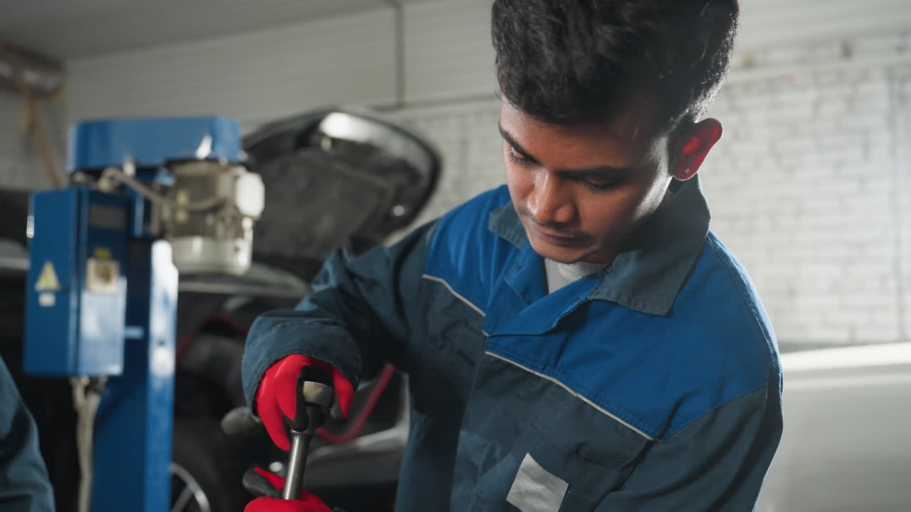 ingeniero centrado en trabajar con el motor del automóvil mientras la maquinaria es visible en el fondo, vista parcial de otra persona en la escena, taller automotriz con herramientas y equipos en uso