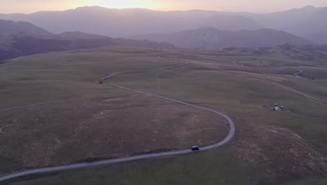 Wide-shot-of-Motorhome-driving-on-small-road-during-sunset-at-Durmitor-National-Park-Montenegro,-aerial