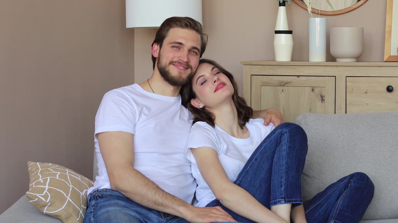 Giovane coppia felice che si abbraccia e sorride sul divano di casa