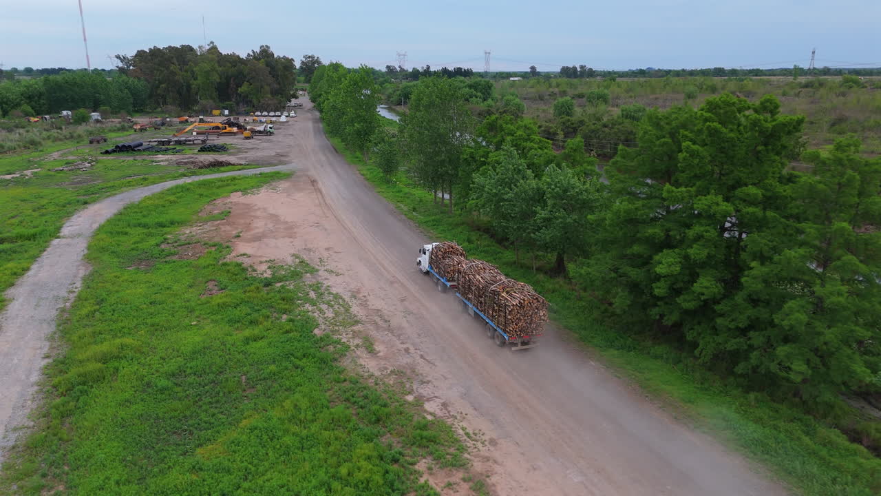 A truck transporting a load of wooden logs along a dirt road through a rural landscape