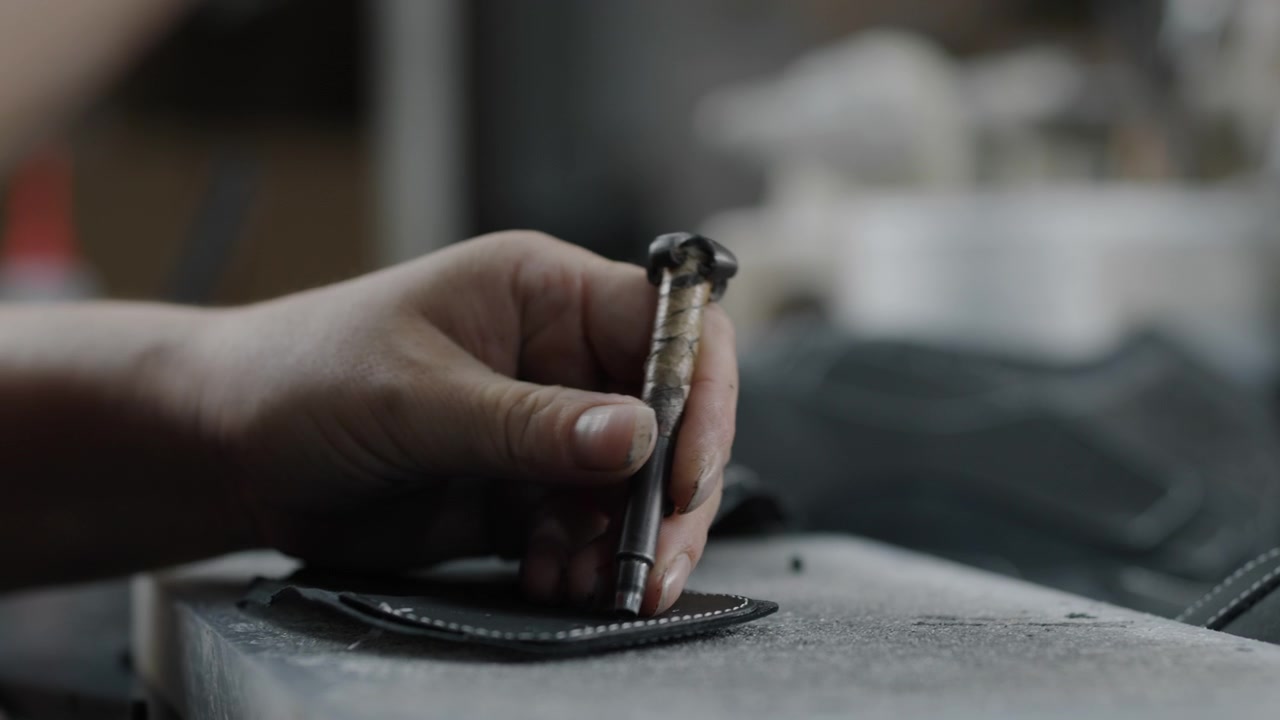 Worker handcrafting leather shoe parts with hand tool in workshop closeup