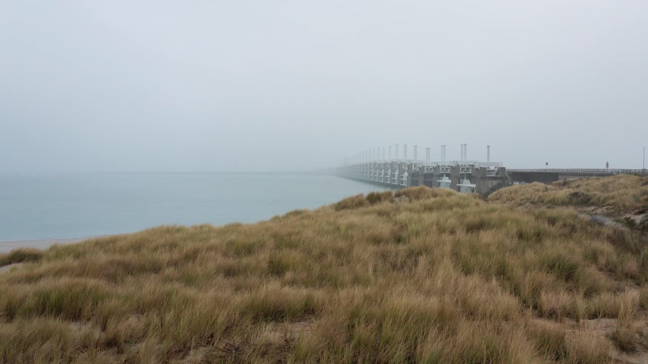Drone flying above the dunes revealing the storm surge barrier located in the Netherlands