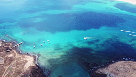 Island-of-Los-Lobos,-aerial-view-of-crystal-blue-water-in-various-shades