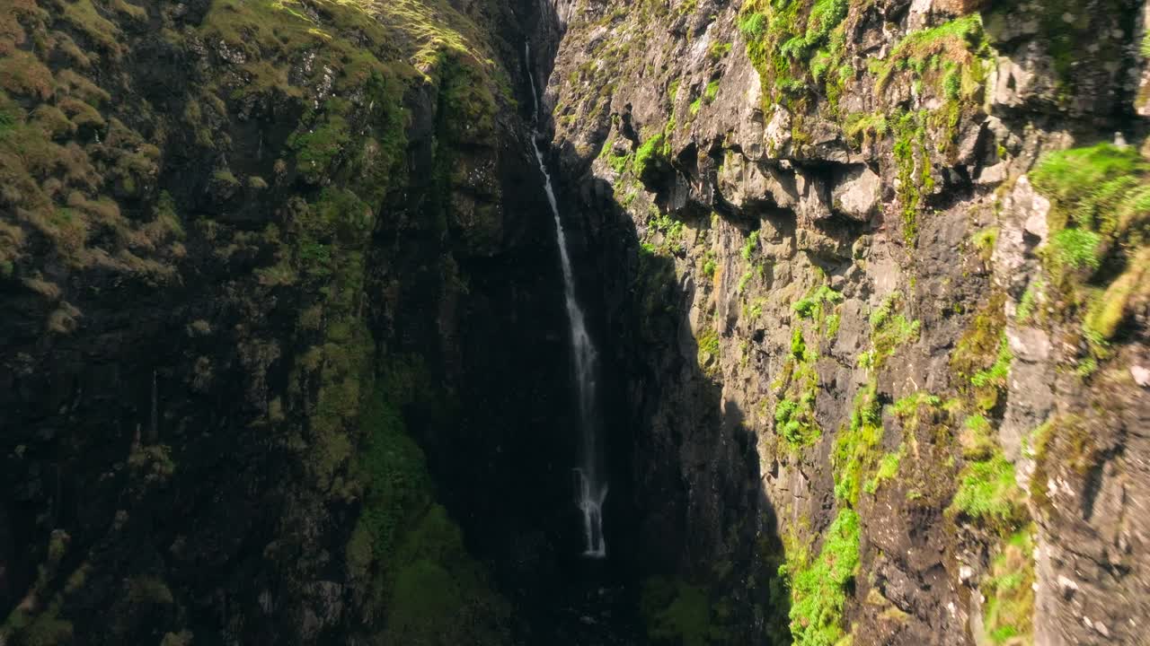 una estrecha cascada fluye por un acantilado rocoso en las islas feroe, rodeada de musgo