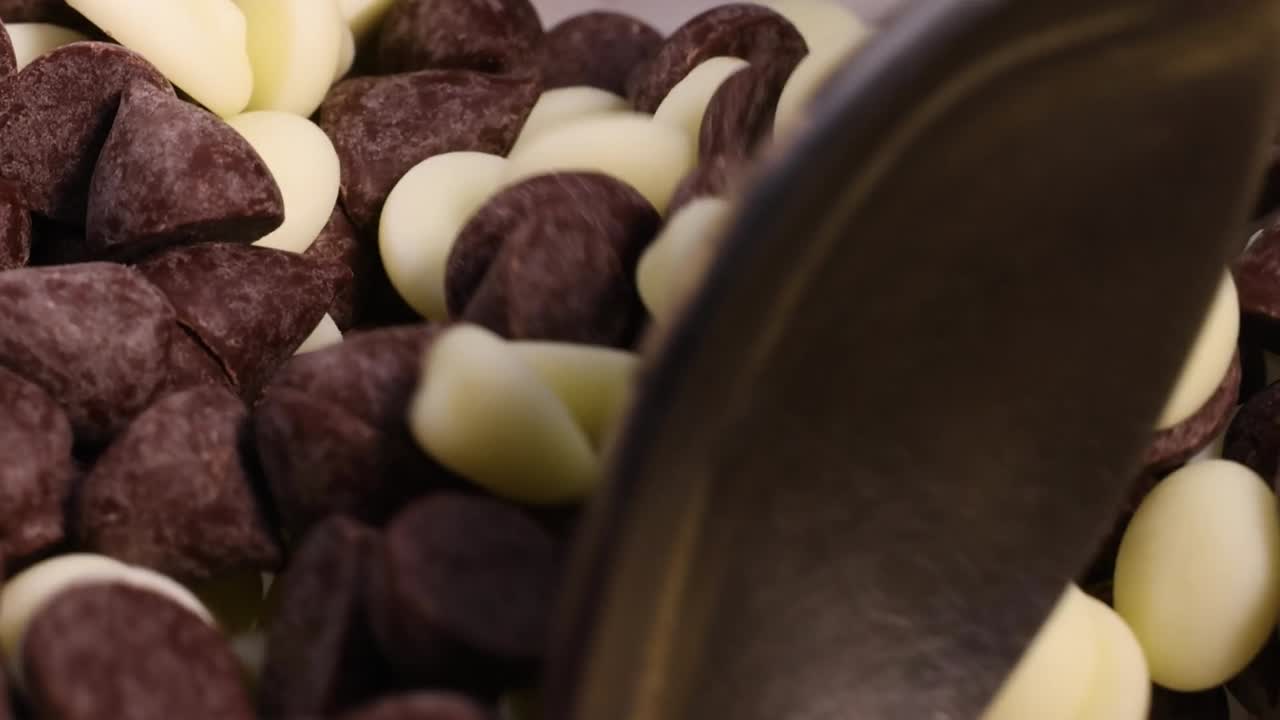 Un cucchiaio di metallo mescola un contrastante mix di gocce di cioccolato fondente e bianco