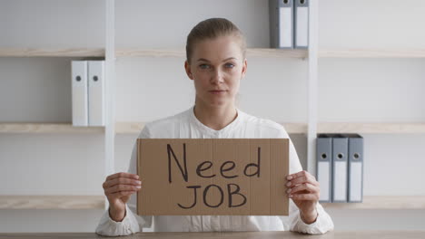 woman holding a "need job" sign in an office