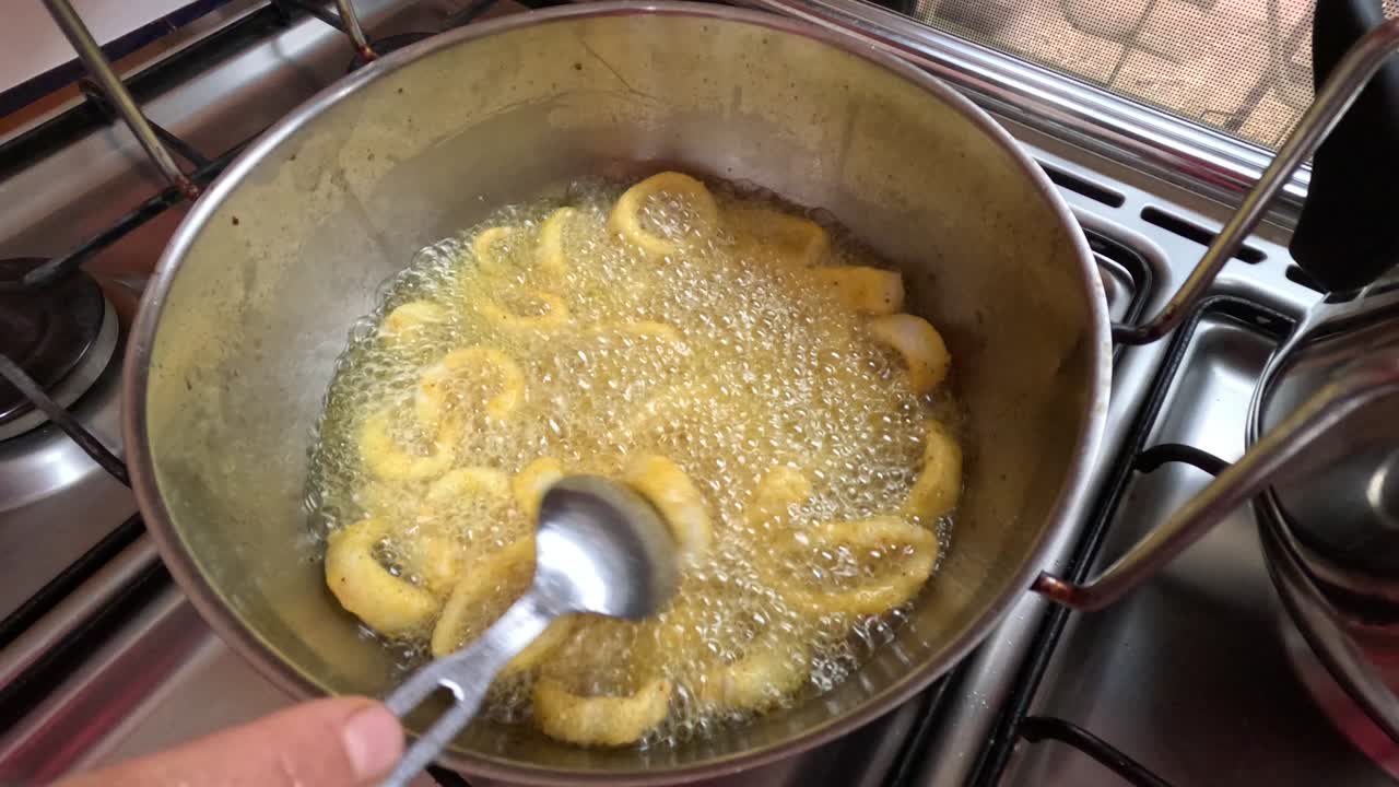 Anelli di calamari marocchini croccanti vengono fritti in olio bollente e ricoperti di pastella aromatizzata durante la preparazione tradizionale di frutti di mare. Una schiumarola solleva gli anelli appena cotti dall'olio caldo mentre ad
