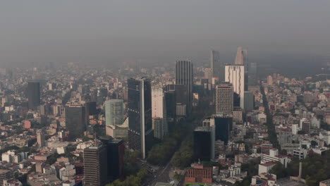 Elevated-panning-view-of-tall-office-building-in-downtown.-Limited-visibility-due-to-air-pollution.-Orbiting-around-group-of-skyscrapers.-Mexico-City,-Mexico.