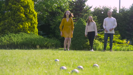 vergezicht van twee blanke jonge vrouwen en een man die petanque speelt in het park op een zonnige dag