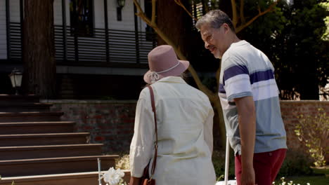 Happy-diverse-senior-couple-walking-with-luggage-to-a-house-in-sunny-outdoors