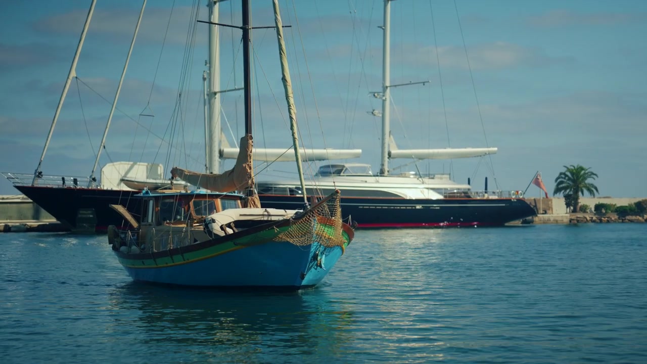 Barca di legno colorata che passa accanto a un grande superyacht di lusso ormeggiato in un porto tranquillo in una giornata di sole.