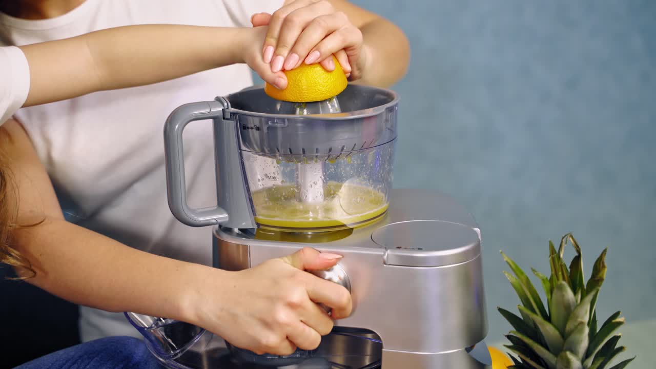 Mother and daughter doing fresh orange juice together. Woman and a little girl making orange drink in the squeezer machine on the table.