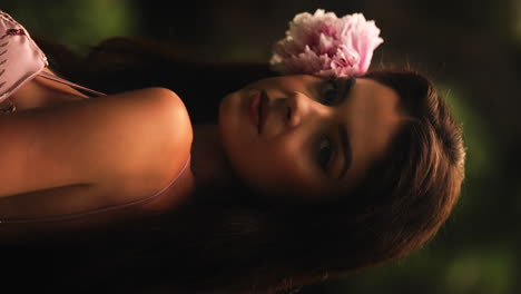 Vertical-shot-of-a-young-woman-posing-with-pink-flower-in-her-hair