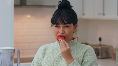 woman in kitchen happy while eating strawberry