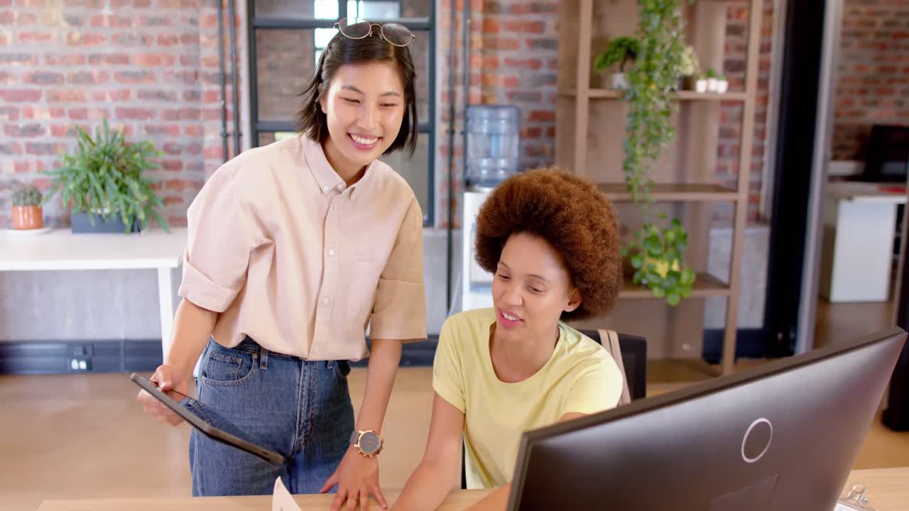 due felici e diverse colleghe creative in una discussione casuale alla scrivania in ufficio, slow motion