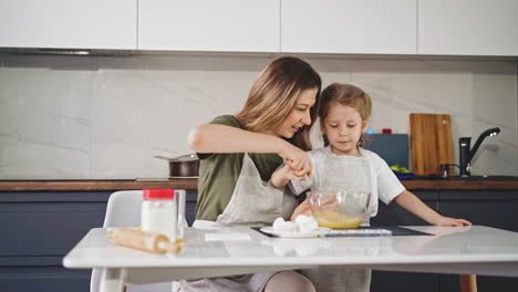 mujer con hija en delantales azota el huevo en el plato en la mesa