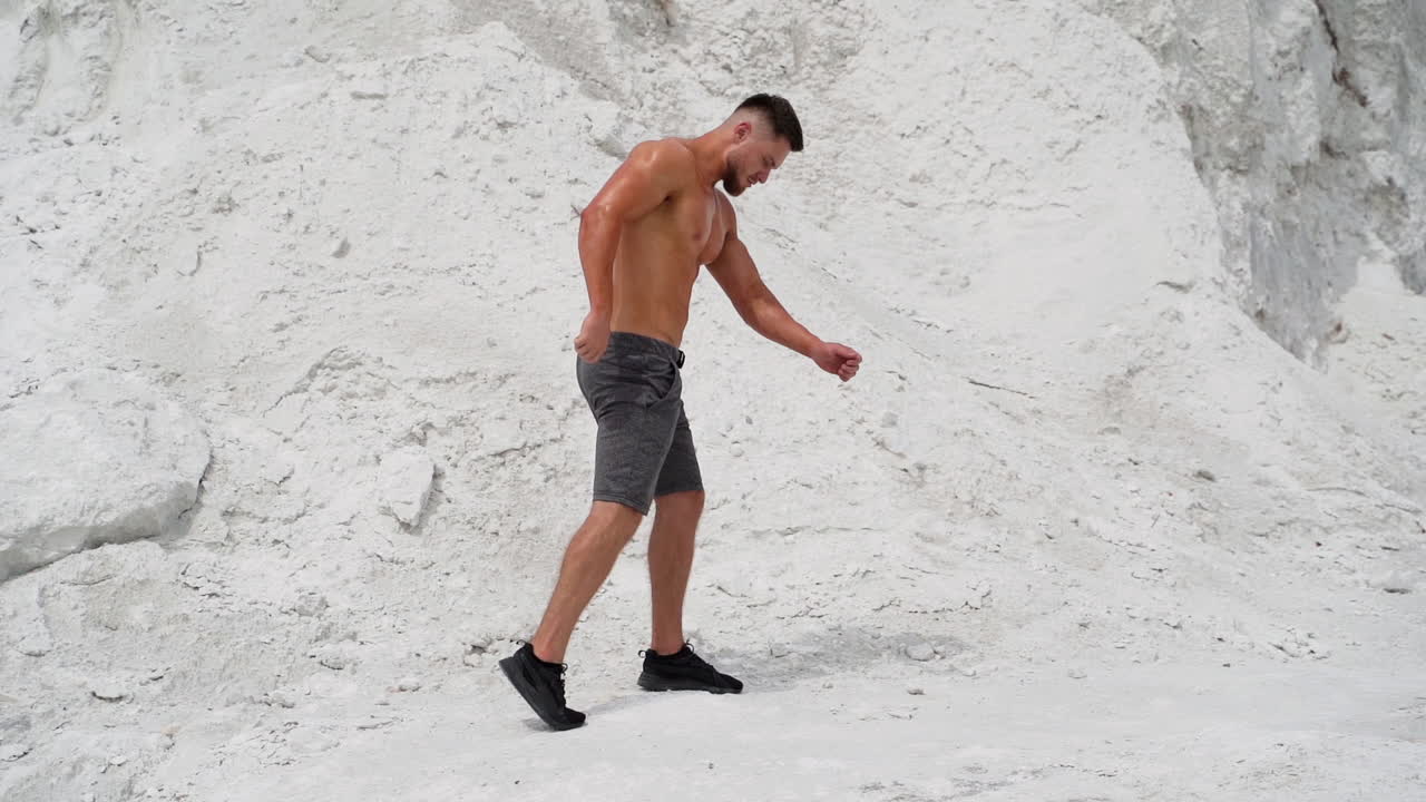 Full-length portrait of a bodybuilder outdoors. Young man with muscular body posing to camera on white mountain background.