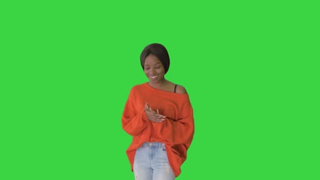 cheerful african american woman wearing bright sweater and jeans talking to the camera on a green screen, chroma key