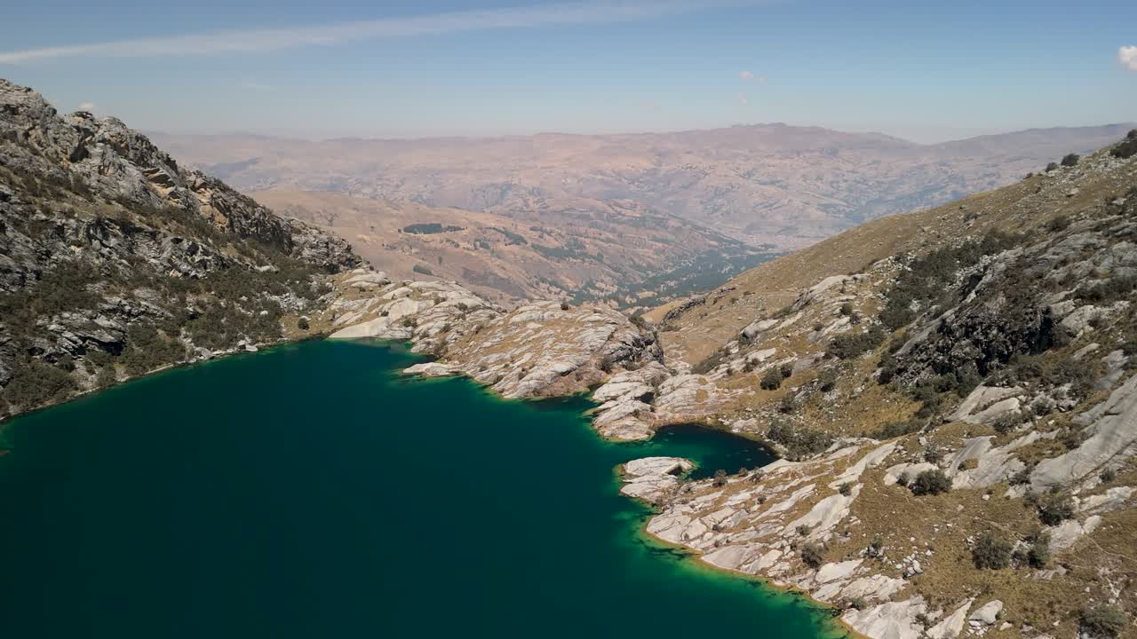 A stunning aerial panorama shot pans across the breathtaking turquoise waters of Laguna Churup, a high-altitude alpine lake nestled in the rocky mountains of Peru's Huascarán National Park